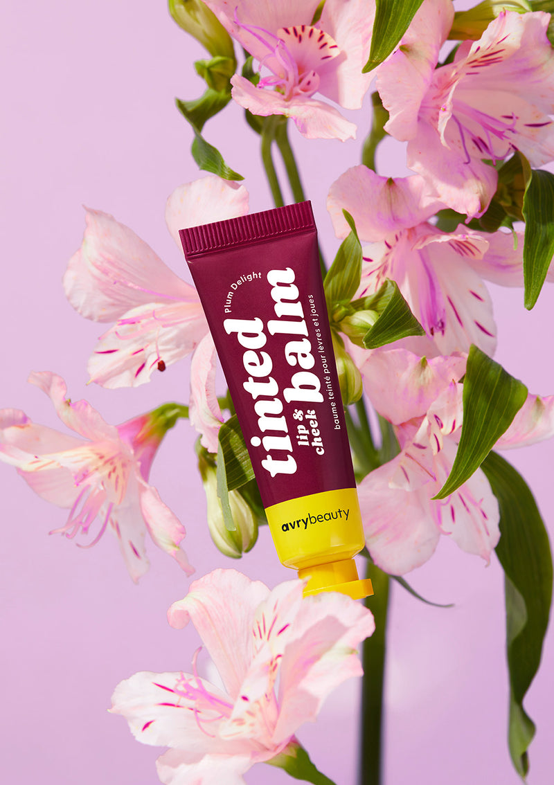 AvryBeauty’s Plum Delight Lip & Cheek Tinted Balm vegan makeup displayed on top of a purple floral background.